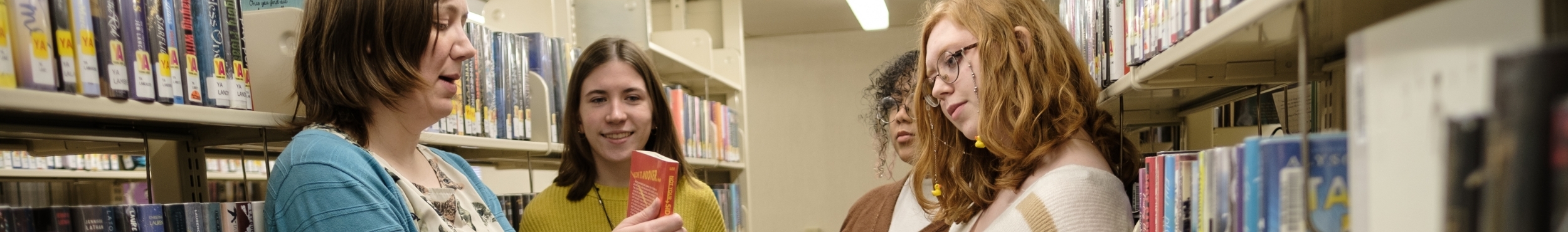 Group of teens talking to librarian in the stacks