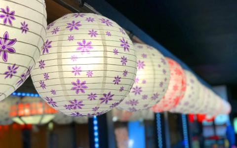White paper lanterns painted with various colors and patterns appear lit up at night.