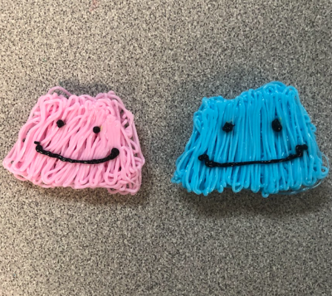 Two Ditto, one pink and one blue, each made of 3-D pen filament, sit on a gray table.