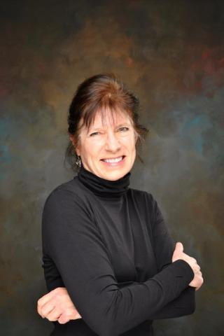 photograph of Dr. Cathy Rosenbaum where black sweater and smiling in front of backdrop.