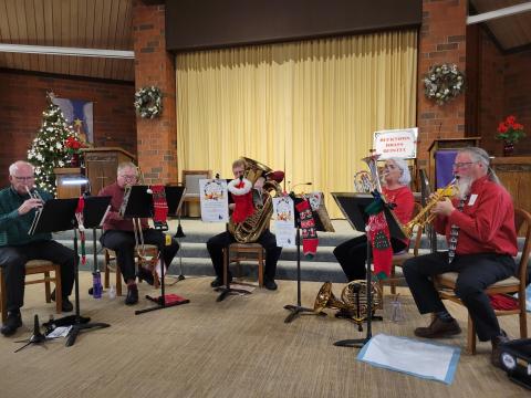 Image of five musical performers playing their brass instrument with christmas tree in background.