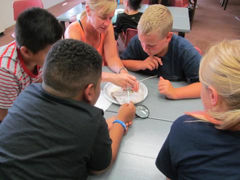 group of kids in blue shirts surrounding a dissection specimen at a library dissection day event. 