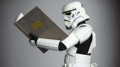 A Stormtrooper reading a large book that says "Star Wars" on the cover.