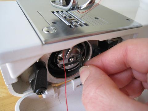 close up image hand threading bobbin case in sewing machine